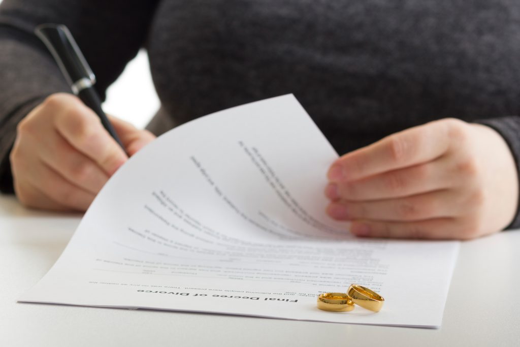 Hands of wife, husband signing decree of divorce, dissolution, canceling marriage, legal separation documents, filing divorce papers or premarital agreement prepared by lawyer. Wedding ring
